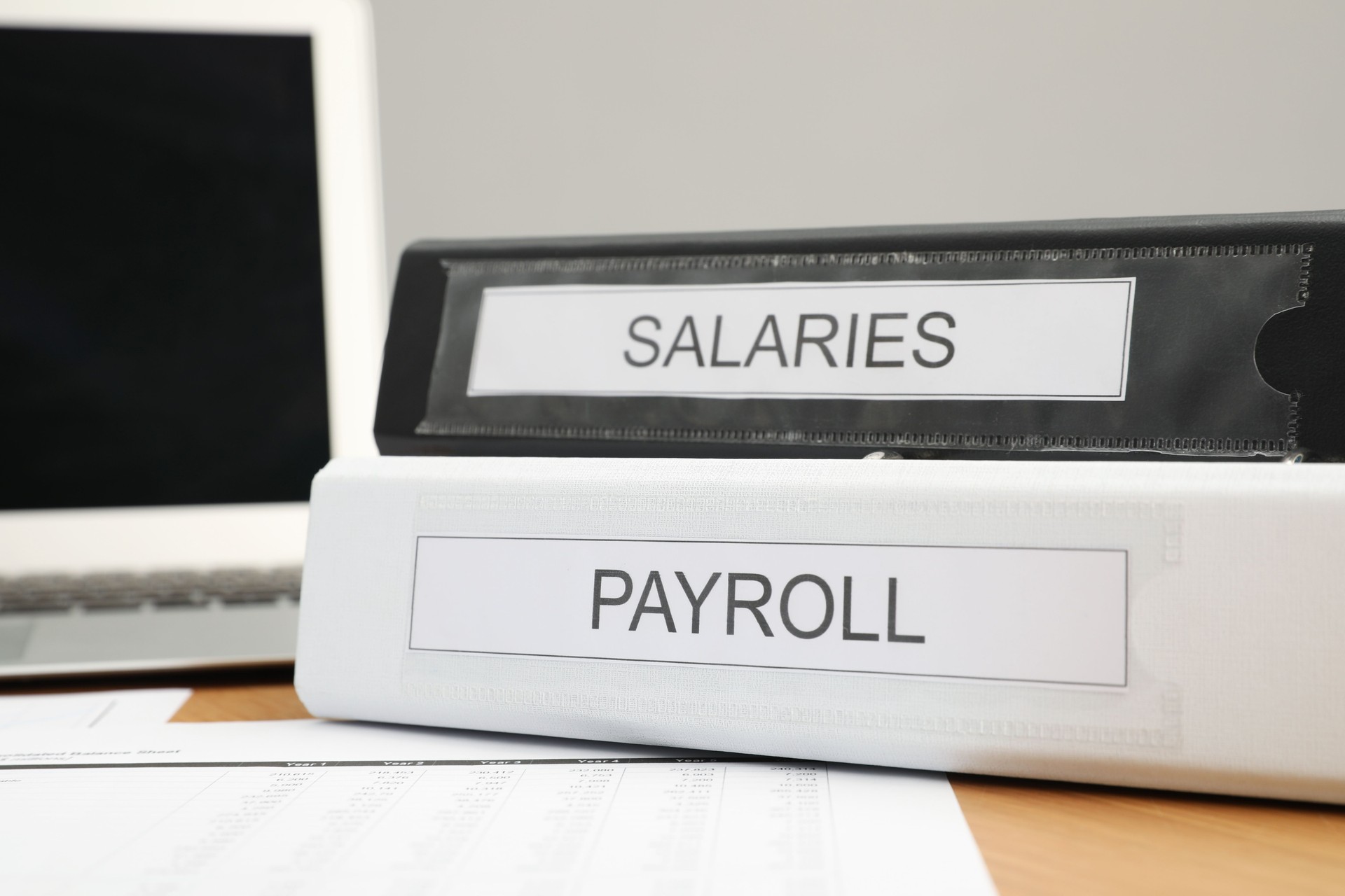 Payroll. Folders, documents and laptop on wooden table, closeup